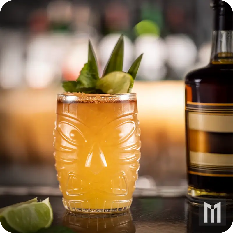 Classic Mai Tai cocktail recipe served in a tiki glass with dark rum float, pineapple garnish, and a bottle of aged rum in the background. A traditional Hawaiian-inspired drink created by Trader Vic.
